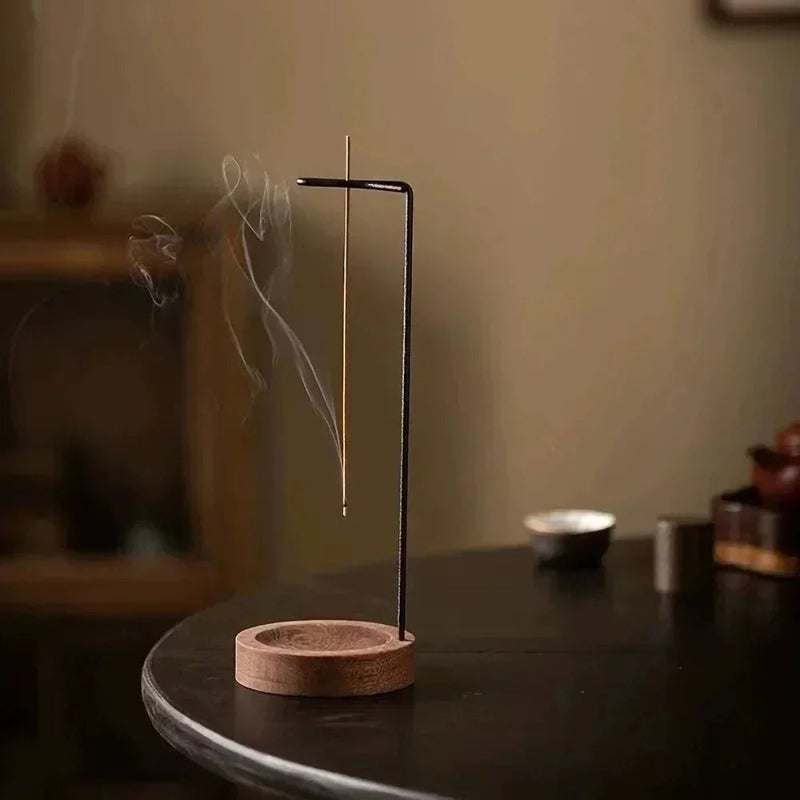 A single burning incense stick on a wooden and black metal holder.