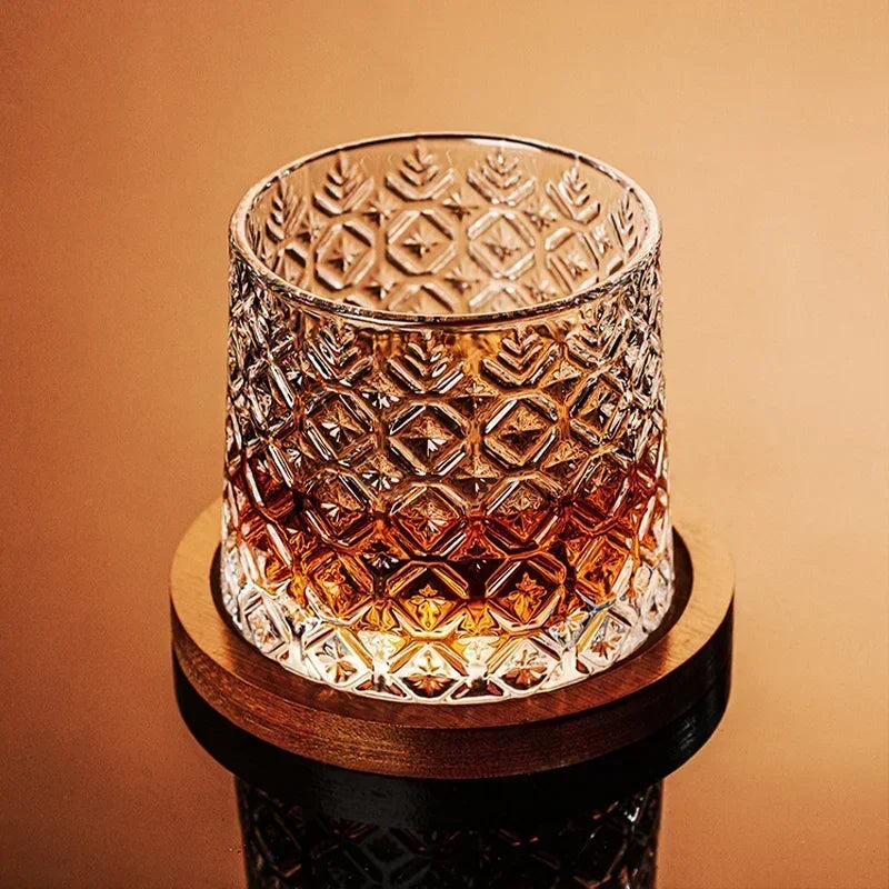 A single cut-crystal whiskey glass filled with amber liquid rests on a wooden coaster.