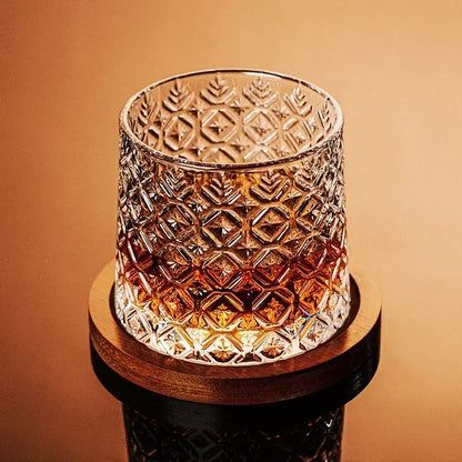 A single cut-crystal whiskey glass filled with amber liquid rests on a wooden coaster.