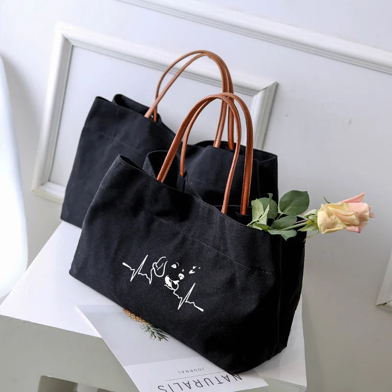 Two black canvas tote bags, one with a white dog and heartbeat graphic.