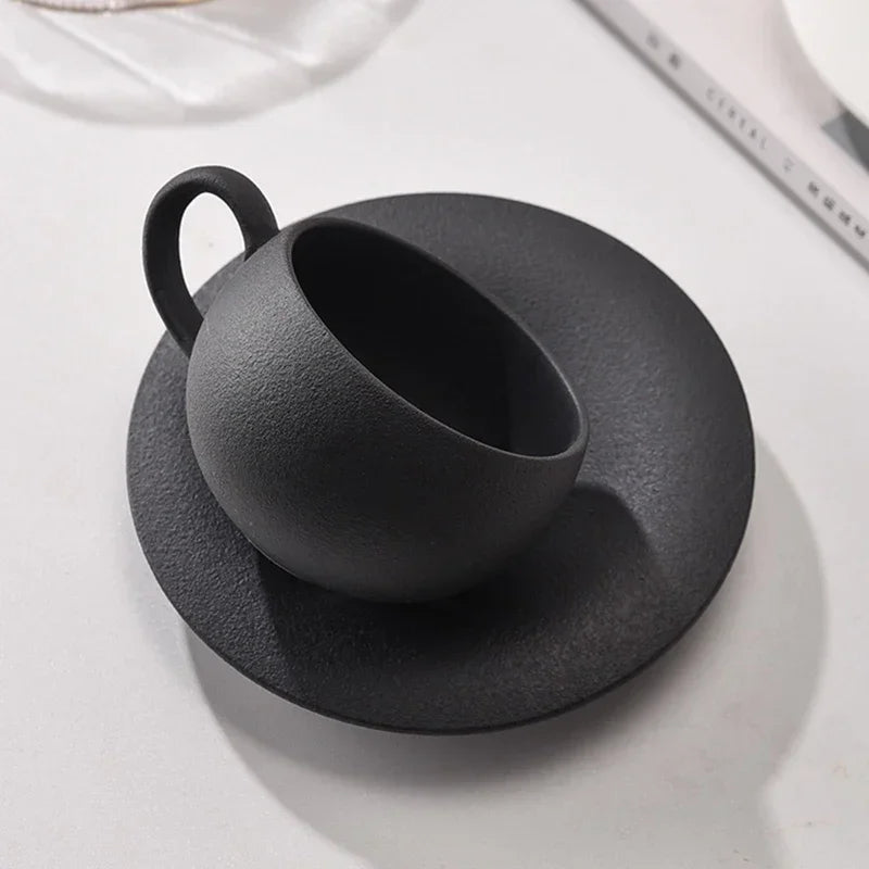A black textured coffee cup tilted on its matching saucer.