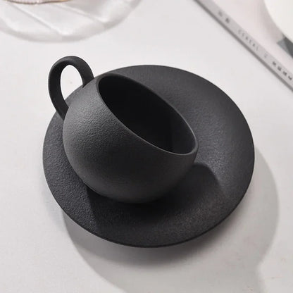 A black textured coffee cup tilted on its matching saucer.
