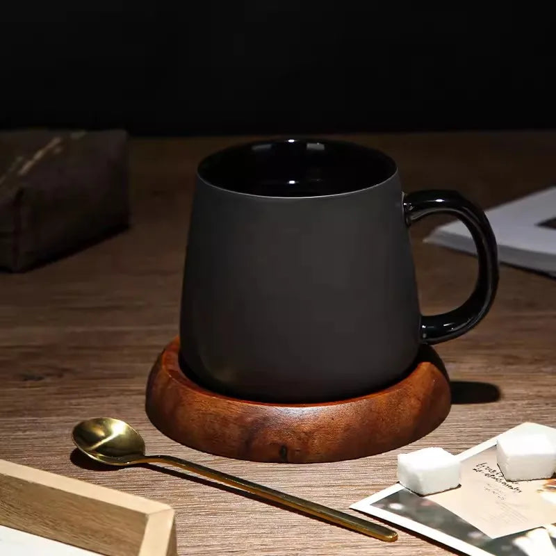 A black mug on a wooden coaster with a gold spoon and sugar cubes.