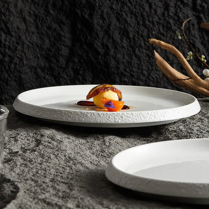 Minimalist white porcelain plate with a textured stone-like edge, elegantly showcasing a gourmet dish against a dark, textured background.