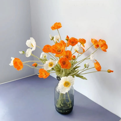 A bouquet of white and orange poppies sits in a gray vase on a blue surface.