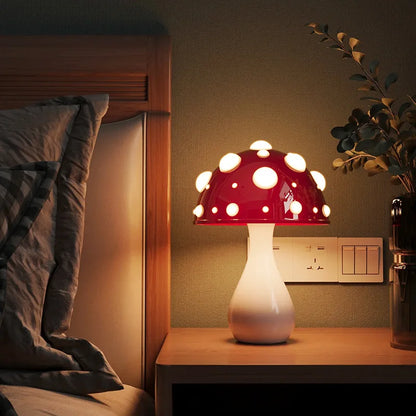 A whimsical mushroom lamp with a red spotted cap and white stem illuminating a bedside table next to a bed.