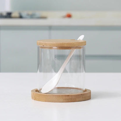 An empty cylindrical glass jar with a wooden lid, spoon, and bamboo coaster.