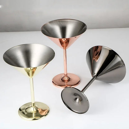 Three metal martini glasses in gold, copper, and black finishes, with one lying on its side.
