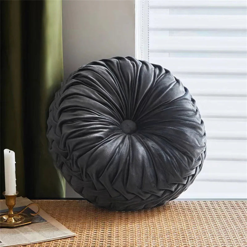 Round gray pillow on a surface with a candle and newspaper in the background
