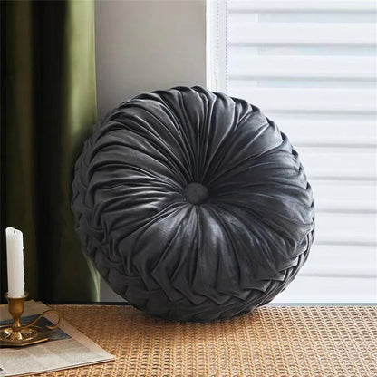 Round gray pillow on a surface with a candle and newspaper in the background