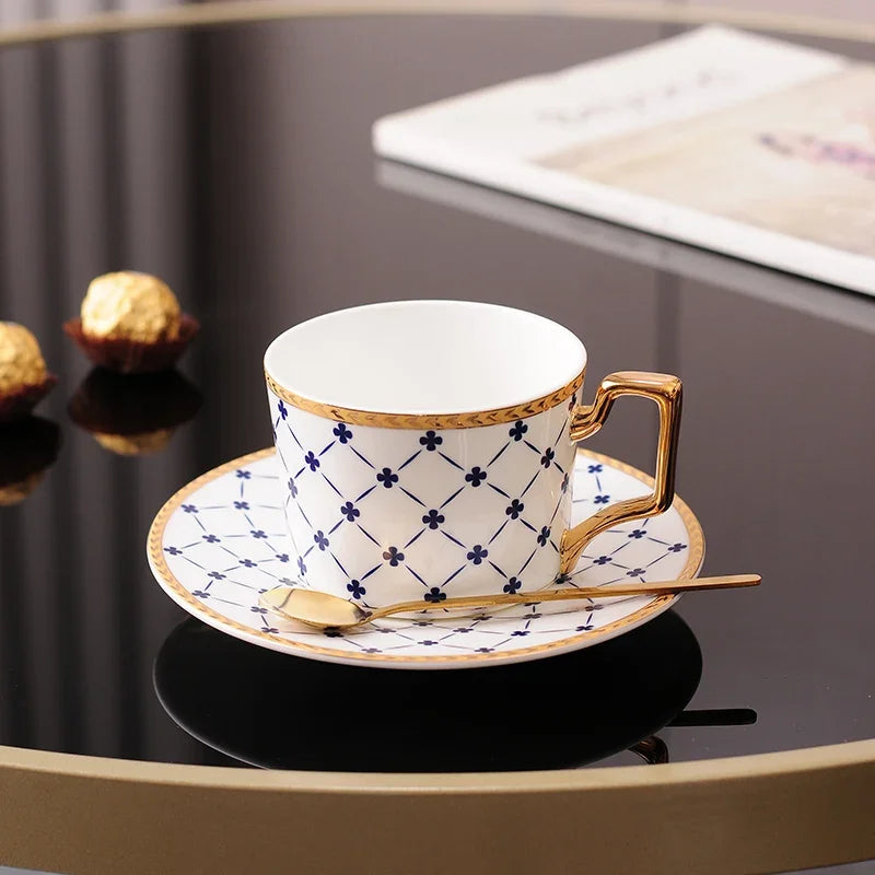 White tea cup and saucer with a blue lattice and clover pattern, and gold trim.