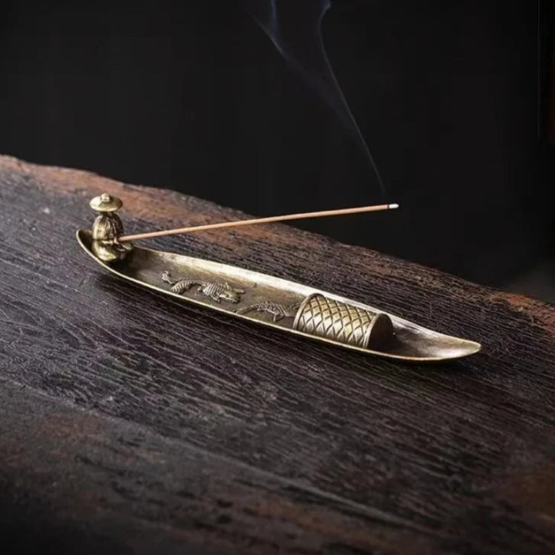 Brass incense burner with incense stick on a dark wooden surface