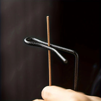 A hand places an incense stick into a black metal holder.
