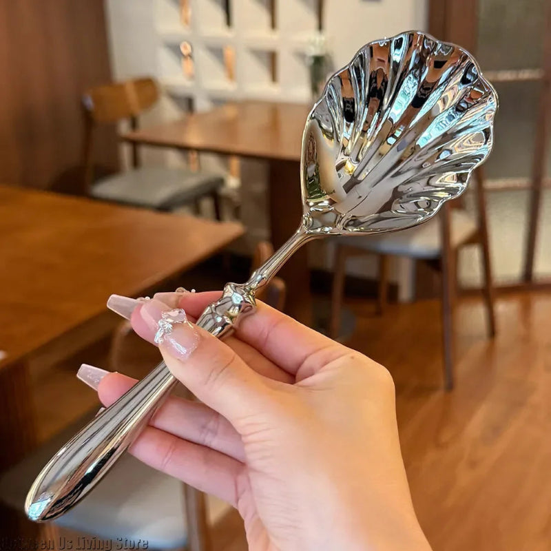 A hand holding a single, polished silver serving spoon with a scalloped, shell-shaped head.