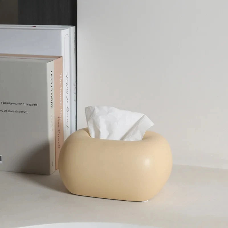 A donut-shaped, tissue box holder sits on a counter next to a stack of books.