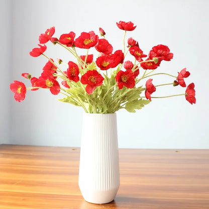 A white ribbed vase holds a bouquet of red poppies on a wooden surface.