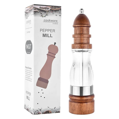 Wooden pepper mill with clear glass body next to its packaging on a white background