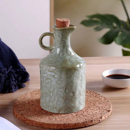Green ceramic bottle with cork stopper on a cork coaster on a wooden surface.