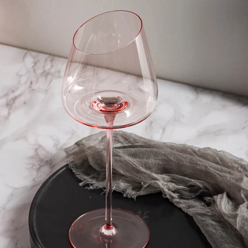 A single clear wine glass with a pink stem and an angled rim, on a black plate.