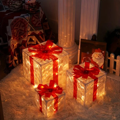 Three clear, illuminated gift boxes with red bows sit on a fluffy white rug, casting a warm glow in a dimly lit room decorated for Christmas.