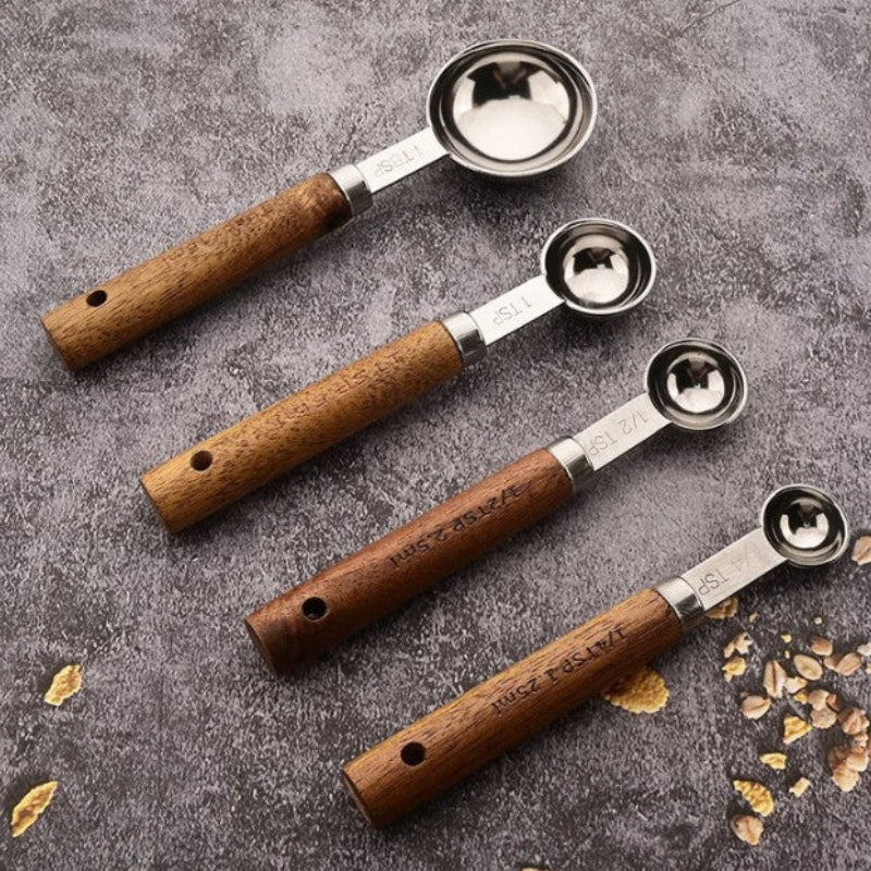 Set of four wooden-handled metal measuring spoons on a textured surface.
