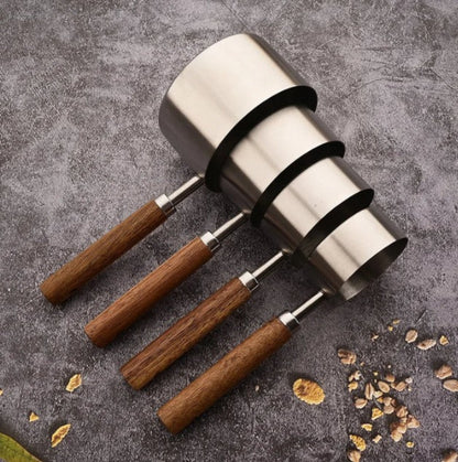 Three metal measuring cups with wooden handles on a gray surface