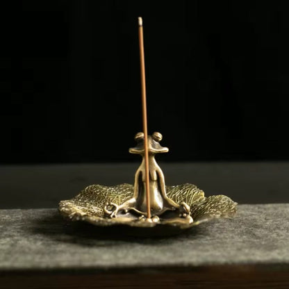 Brass incense holder with a single incense stick on a dark background