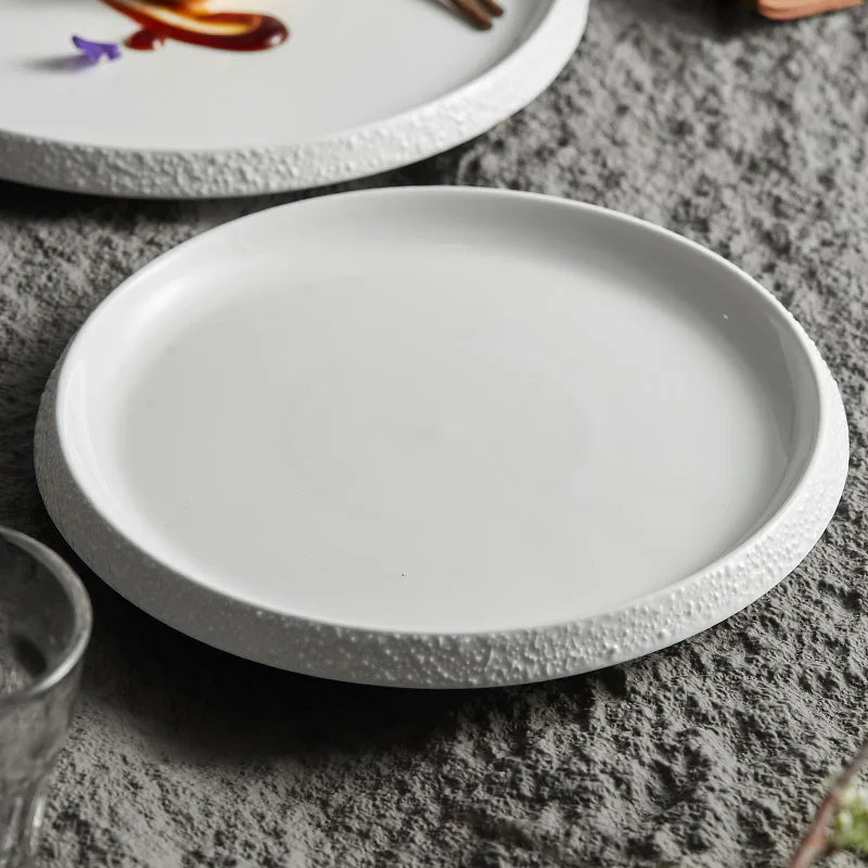 A sleek white stoneware plate with a subtly textured rim, placed on a rustic stone surface, perfect for modern and minimalist table settings.