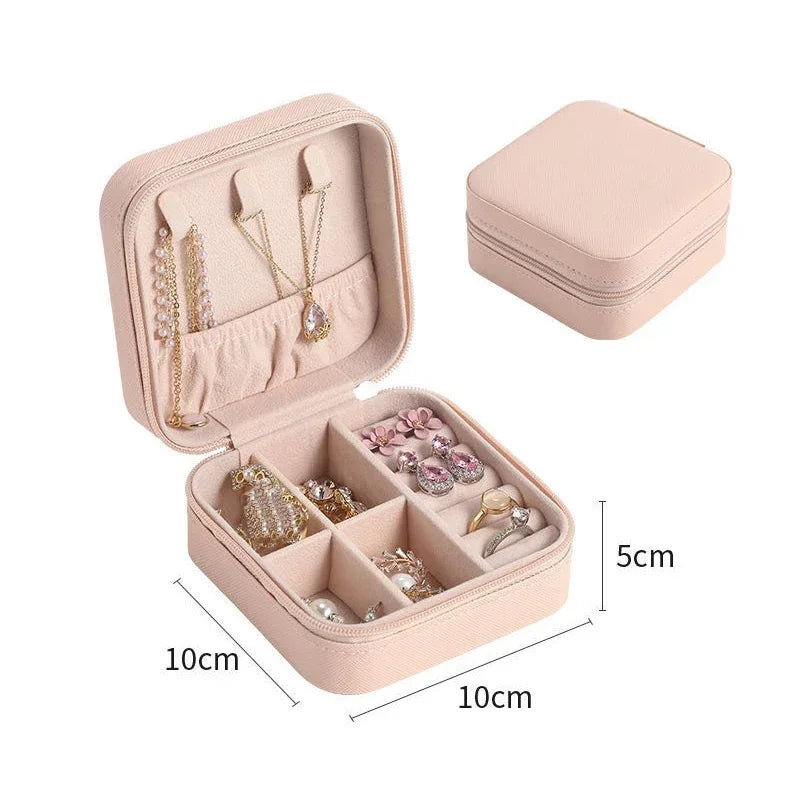 An open pink square jewelry box filled with various necklaces, earrings, and rings, with a closed matching box in the background, showing dimensions of 10cm x 10cm x 5cm.