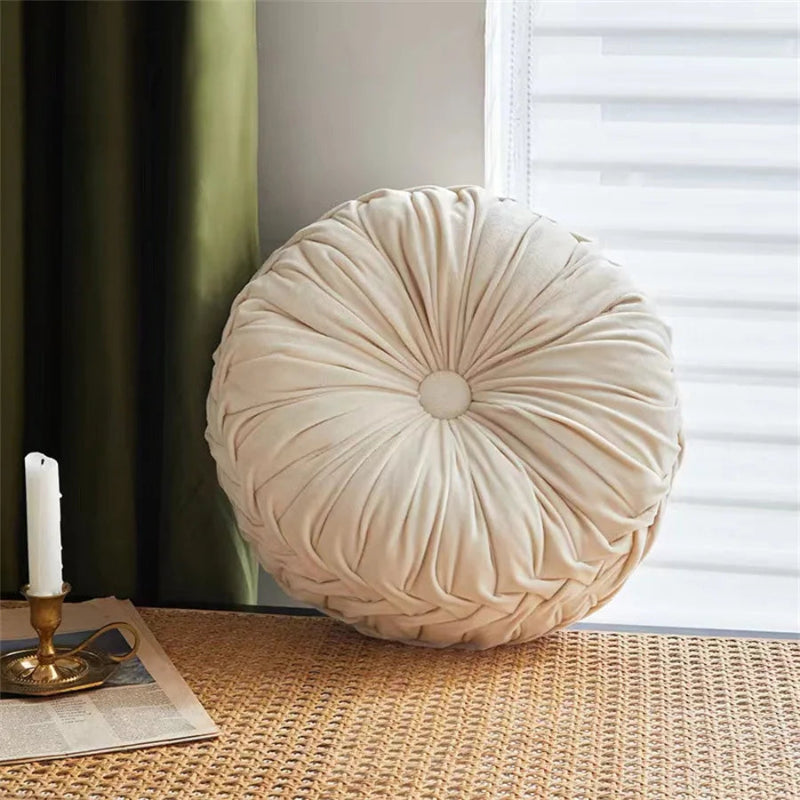 Round beige pillow on a table with a candle and newspaper in the background
