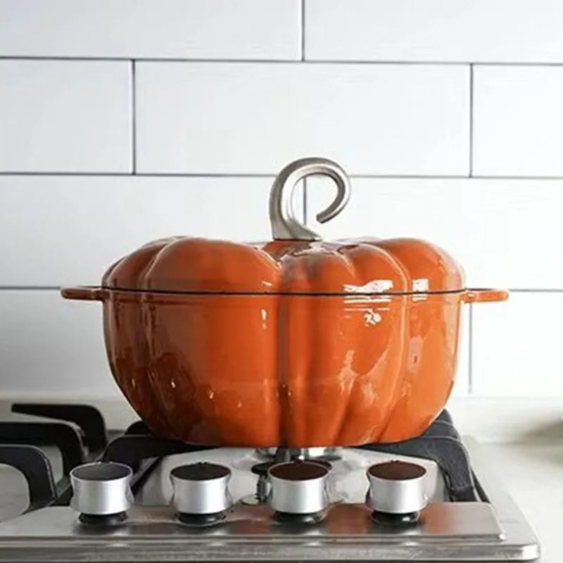An orange, pumpkin-shaped cast iron pot with a gray handle sits on a stovetop with a white tiled backsplash.