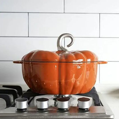 An orange, pumpkin-shaped cast iron pot with a gray handle sits on a stovetop with a white tiled backsplash.