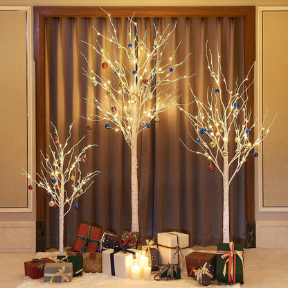 Decorative trees with lights and ornaments in a room with gift boxes and candles.