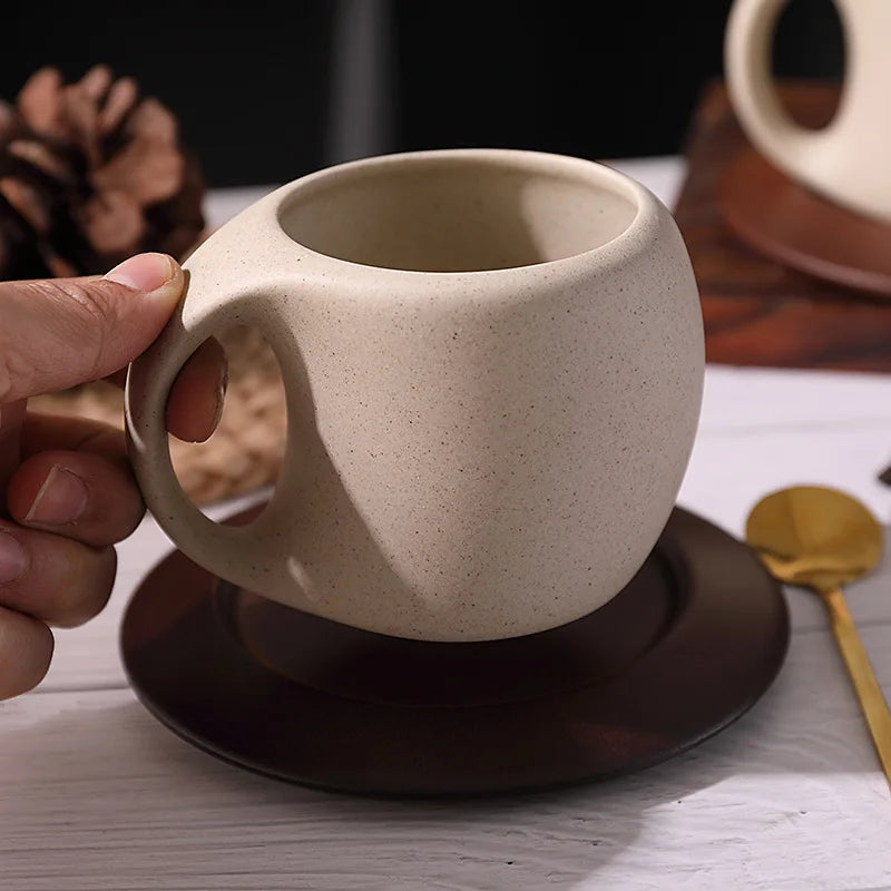 A hand holding a rustic coffee cup with a wooden saucer.
