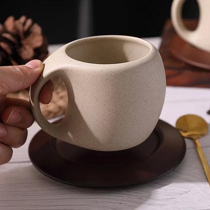 A hand holding a rustic coffee cup with a wooden saucer.