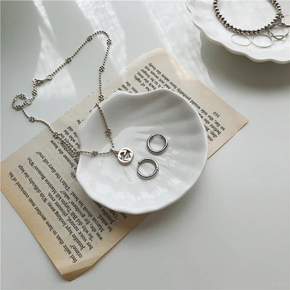 Silver jewelry in a white shell-shaped dish on a piece of paper.