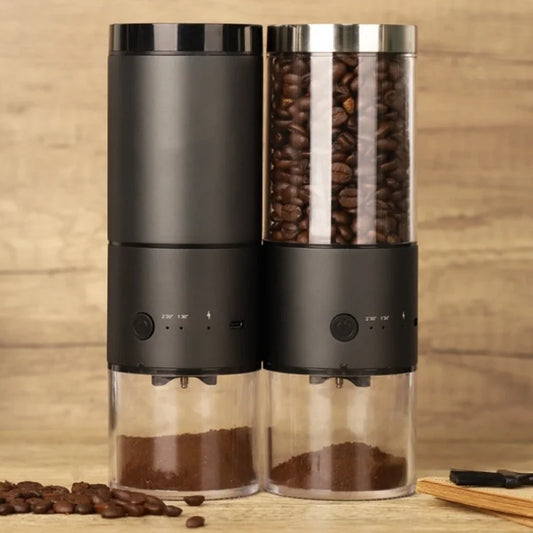 Two modern electric coffee grinders with a sleek black design, displayed side by side. One grinder has a transparent bean hopper filled with coffee beans, while both have clear lower chambers containing freshly ground coffee. The wooden background and scattered coffee beans create a warm and inviting coffee-making scene.