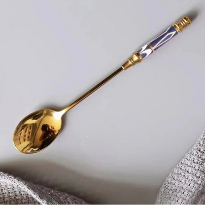 Gold spoon with decorative handle on a light gray background