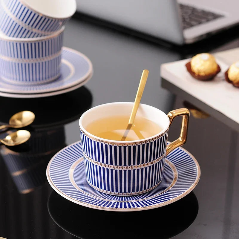 Blue and white striped tea cup and saucer with gold trim, containing tea, and a gold spoon.
