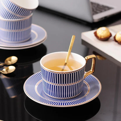 Blue and white striped tea cup and saucer with gold trim, containing tea, and a gold spoon.