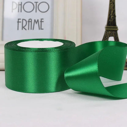 Green satin ribbon with a roll and a few strands on a light surface.