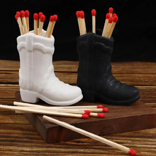 White and black boot-shaped match holders with matches on a wooden surface.