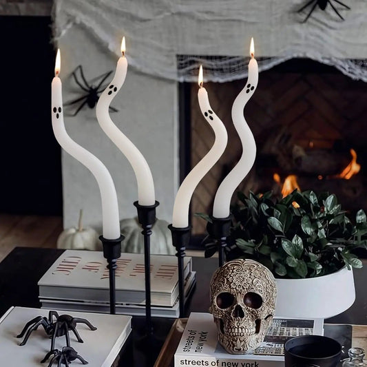 Decorative candles with ghost shapes, skull, and spider decorations on a table in front of a fireplace.