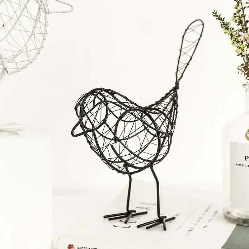 Black wire bird sculpture on a white surface with a vase and plant in the background