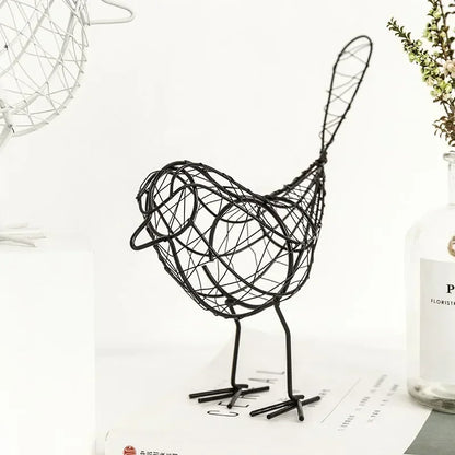 Black wire bird sculpture on a white surface with a vase and plant in the background