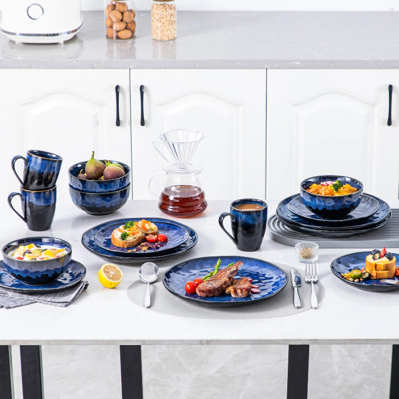 A table is set with a complete dinnerware set of vibrant blue plates, bowls, and mugs, with plates of various foods.