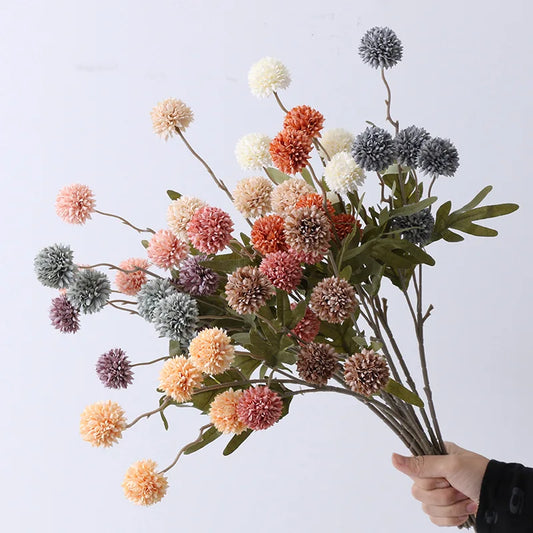 A hand holds a bouquet of faux dahlia flowers in various pastel colors.