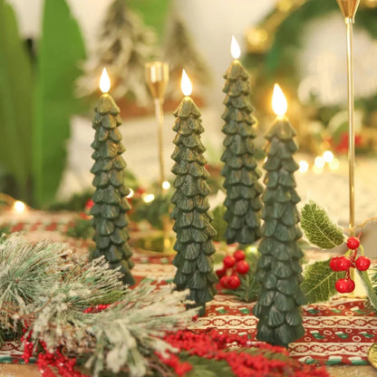 Decorative candles shaped like Christmas trees on a festive table setting with lights and greenery.