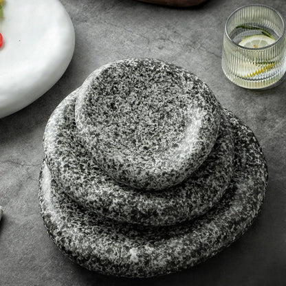 Stack of stone plates on a dark surface with a glass and dish in the background