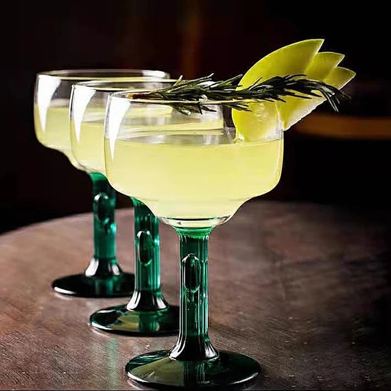 Three green cocktail glasses with yellow cocktails and garnishes on a dark surface.
